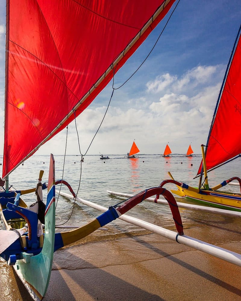 Traditional jukung outrigger boat with a red sail on the shore at Sanur, Bali